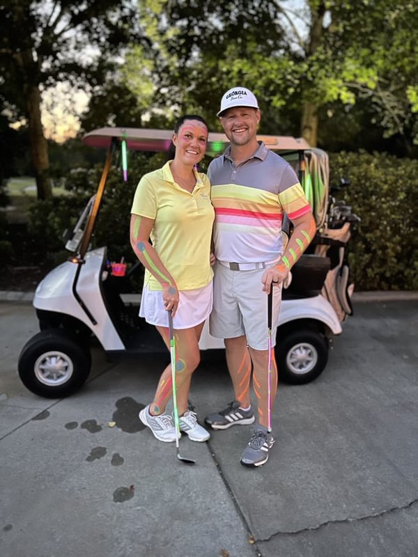 a couple in golf clothes posing in front of a golf card